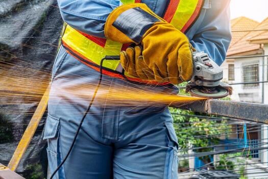 Young man welder in a working blue overall and working gloves grinds a metal object with a angle grinder in the garage bright sparks fly to the sides photo
